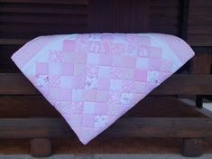 a pink and white quilted baby blanket hanging on a wooden bench