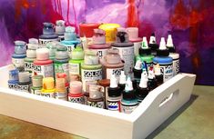 a white tray filled with lots of different colored inks and paint bottles next to a purple wall