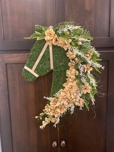 a wreath made out of grass and flowers hanging on a wooden door with bells in front of it