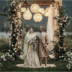 a bride and groom standing in front of an outdoor wedding ceremony arch with chandeliers