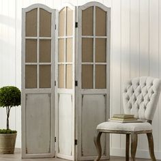 a white chair sitting in front of a tall wooden cabinet next to a potted plant