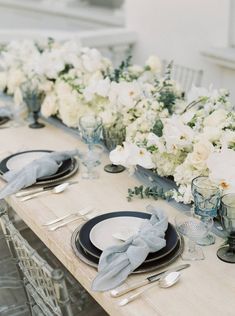 the table is set with white flowers and place settings