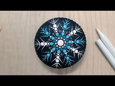 a black and blue painted rock sitting on top of a wooden table next to two white pens