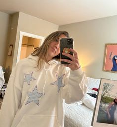 a woman taking a selfie in front of her mirror wearing a white sweatshirt with stars on it