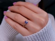 a woman's hand wearing a gold ring with an emerald and blue sapphire stone