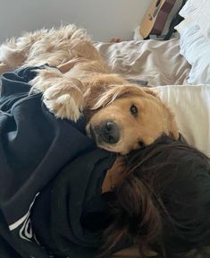 a dog laying on top of a bed next to a person wearing a black shirt