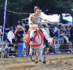 a woman riding on the back of a white horse in front of a group of people