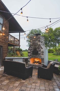 an outdoor fireplace with patio furniture and string lights