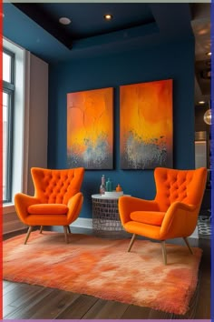 two orange chairs sitting in front of a painting on the wall next to a round table