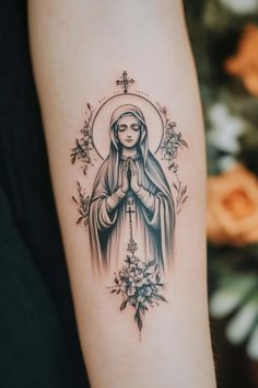 Tattoo of a praying woman with a halo and floral designs on an arm. Rosary Tattoo For Women, Simple Virgin Mary Tattoo, Simple Christian Tattoos For Women, Miraculous Medal Tattoo, Lady Of Guadalupe Tattoo, Virgin De Guadalupe Tattoo Ideas, Religious Tattoos For Women, Jesus Portrait Tattoo, Catholic Tattoo Ideas