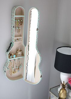 a white wall mounted jewelry case next to a lamp and table with flowers on it