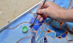 a person using a paintbrush to paint a stained glass piece with blue and green colors