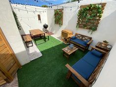 an outdoor living area with green grass and wooden furniture on the floor, along with potted plants