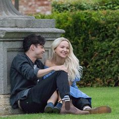 a man and woman sitting on the ground next to a stone pillar smiling at each other