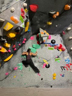 a woman climbing up the side of a rock wall with colorful rocks and boulders in the background