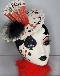 a white mask with red feathers and playing cards on it