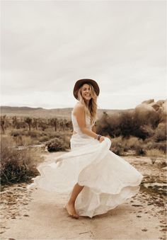 a woman in a white dress and hat is posing for a photo on the desert