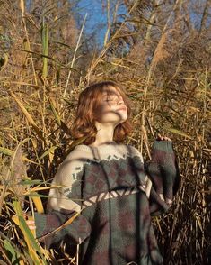 a woman standing in tall grass with her eyes closed and hands up to the sky