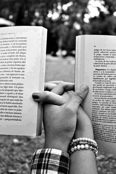 black and white photograph of two hands holding open books in front of each other with trees in the background