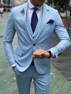 a man in a blue suit and tie is standing on the street with his hands in his pockets