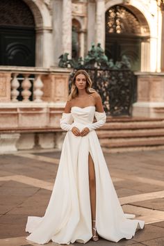 a woman in a white wedding dress standing on the ground with her legs crossed and looking off to the side