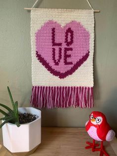 a crocheted heart hanging on a wall next to a potted succulent