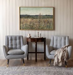 two gray chairs sitting next to each other in front of a painting on the wall