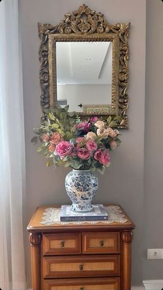 a vase filled with flowers sitting on top of a wooden table next to a mirror