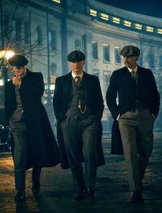 three men in suits and hats are walking down the street at night with their hands on their hips