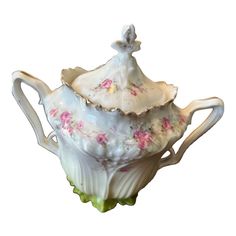 a white tea pot with pink flowers and a lady figurine on the top