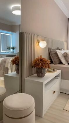 a white bed sitting next to a tall mirror in a bedroom under a ceiling light