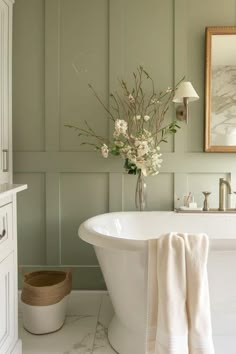 a white bath tub sitting in a bathroom next to a wall mounted mirror and a vase with flowers