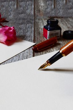 a pen sitting on top of a piece of paper next to some ink and flowers