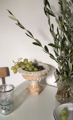 olives in a bowl on a table next to two glasses and an olive branch