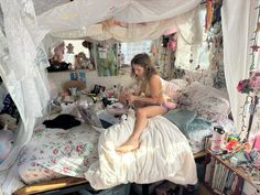 a woman sitting on top of a bed in a room with lots of clutter