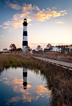 a black and white lighthouse sitting on top of a body of water next to tall grass