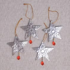 three silver star ornaments hanging from strings on a linen surface with red beads and thread