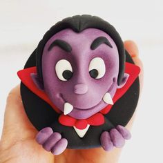 a hand holding a small purple toy with black and red decorations on it's face