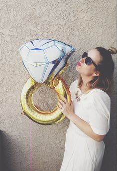 a woman in sunglasses is holding some balloons and posing for the camera next to an image of a diamond ring