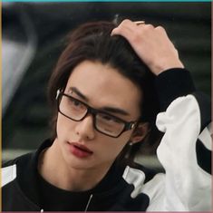 a young man wearing glasses is looking at the camera and has his hand on his head