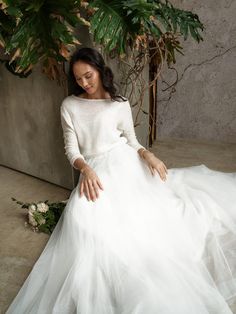 a woman in a white dress sitting on the ground next to a plant and flowers