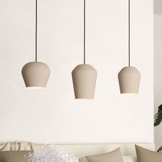 three light fixtures hanging from the ceiling in a living room with white walls and pillows