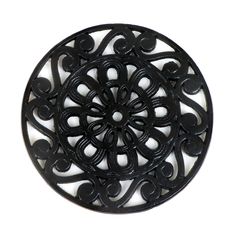 a black circular metal object on a white surface with an intricate design in the center