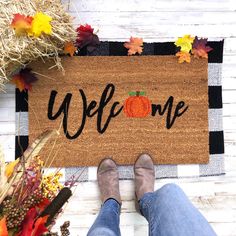 a person standing in front of a welcome mat with pumpkins and hay on it