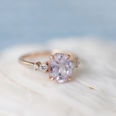 an oval shaped pink sapphire and diamond ring on top of a piece of white sand