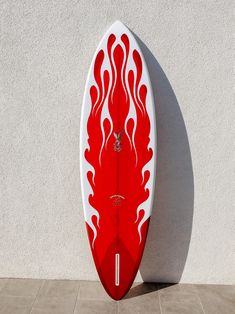 a red and white surfboard sitting against a wall