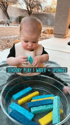 a baby sitting in front of a bowl of sponges with the words sensory play i water and sponges