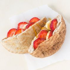 a sandwich with strawberries and bananas on top of it sitting on a piece of paper