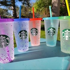 four different colored starbucks cups sitting on top of a blue table with straws in them