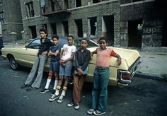 a group of young men standing next to a car on a street with an old building in the background